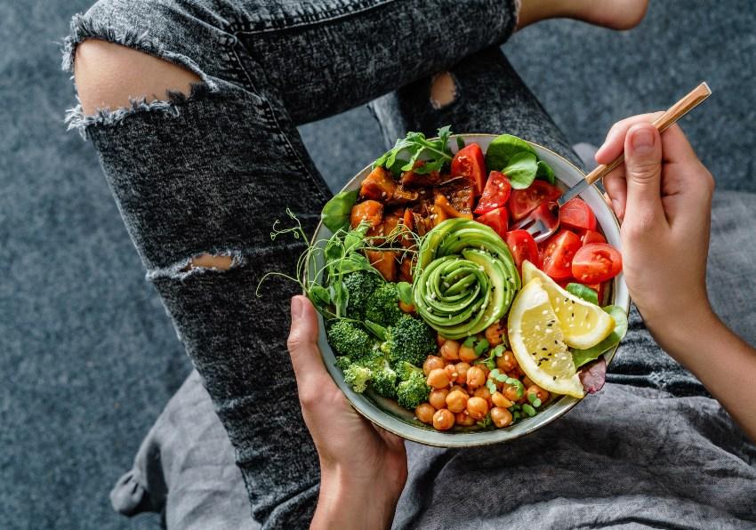 Eine junge Frau lässt sich eine Schale mit Salat und Gemüse schmecken 