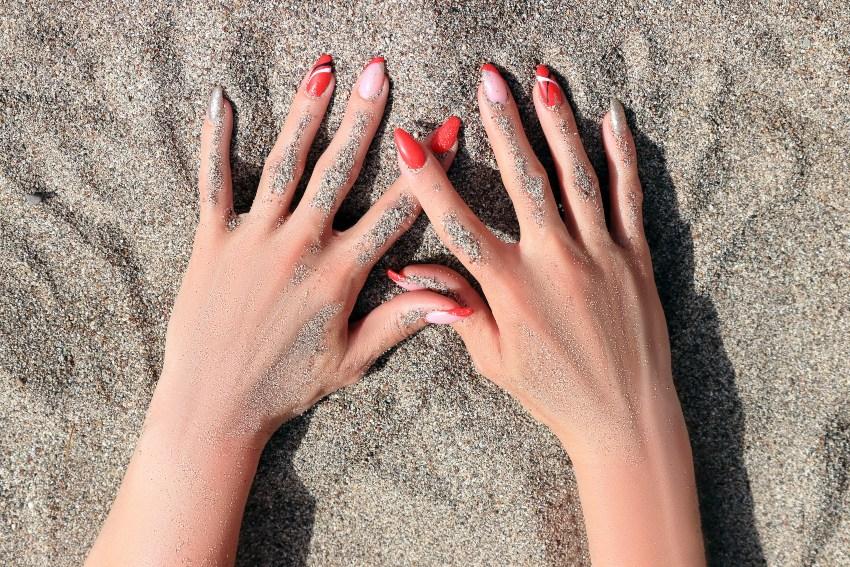 Eine Dame präsentiert ihre wunderschön rotlackierte Fingernägel im am Strand Hautfarbe