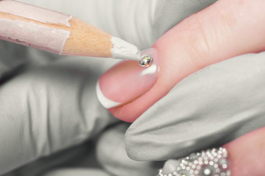 Sorgfältig befestigt ein Nailartist einen Strassstein auf einem Fingernagel Strass