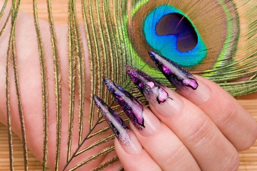 Ein sehr aufwändiges Nageldesign in Stilettoform, im Hintergrund ist eine Pfauenfeder zu sehen 