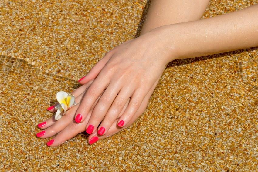 Am Strand präsentiert eine junge Frau ihr Nageldesign in Rottönen