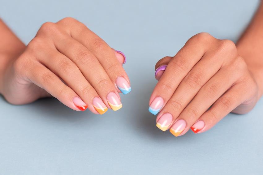 Eine Frau präsentiert ihre French-Nails, jede Nagelspitze ist einer einer Farbe des Regenbogens gefärbt