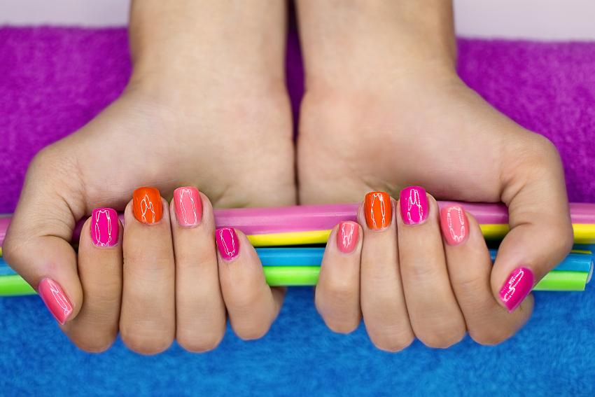 Eine Frau präsentiert ihr Nageldesign, die Nägel glänzen in Pink- und Orangetönen 