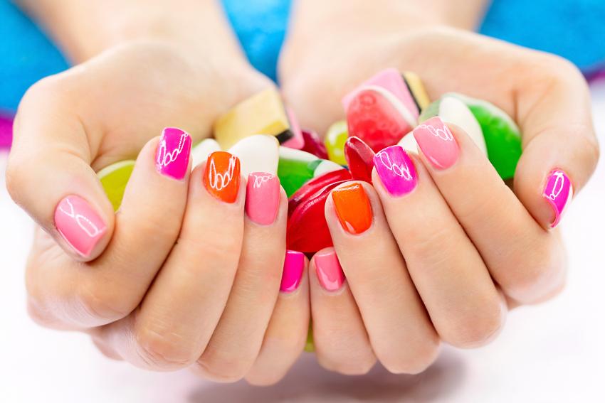 Eine Frau präsentiert ihr Nageldesign, ihre Nägel sind abwechselnd in Pink- und Orangetönen lackiert 
