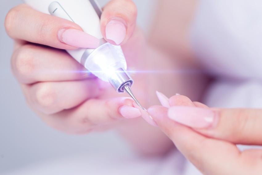 Frau nutzt elektrische Nagelfeile für Maniküre