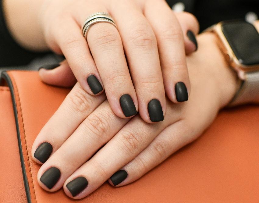 Haende einer Frau mit mattem schwarzen Nagellack - Nageldesign in Schwarz