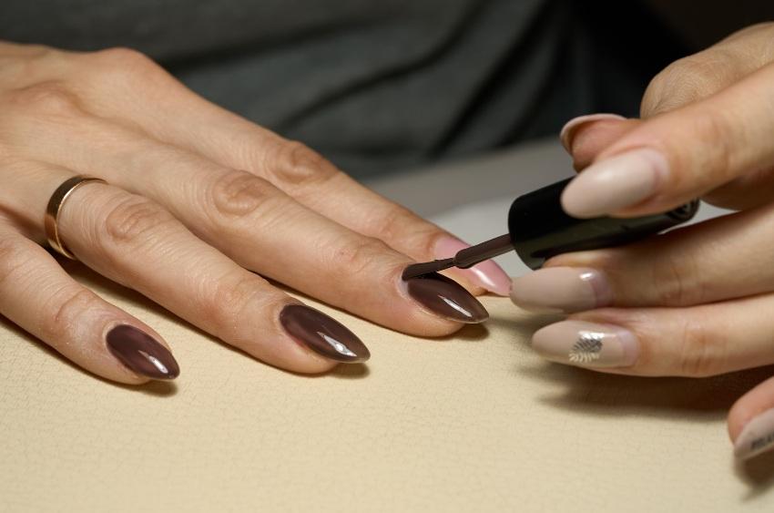 Frau lackiert sich ihre Fingernaegel mit braunem Lack - Nageldesign in Braun